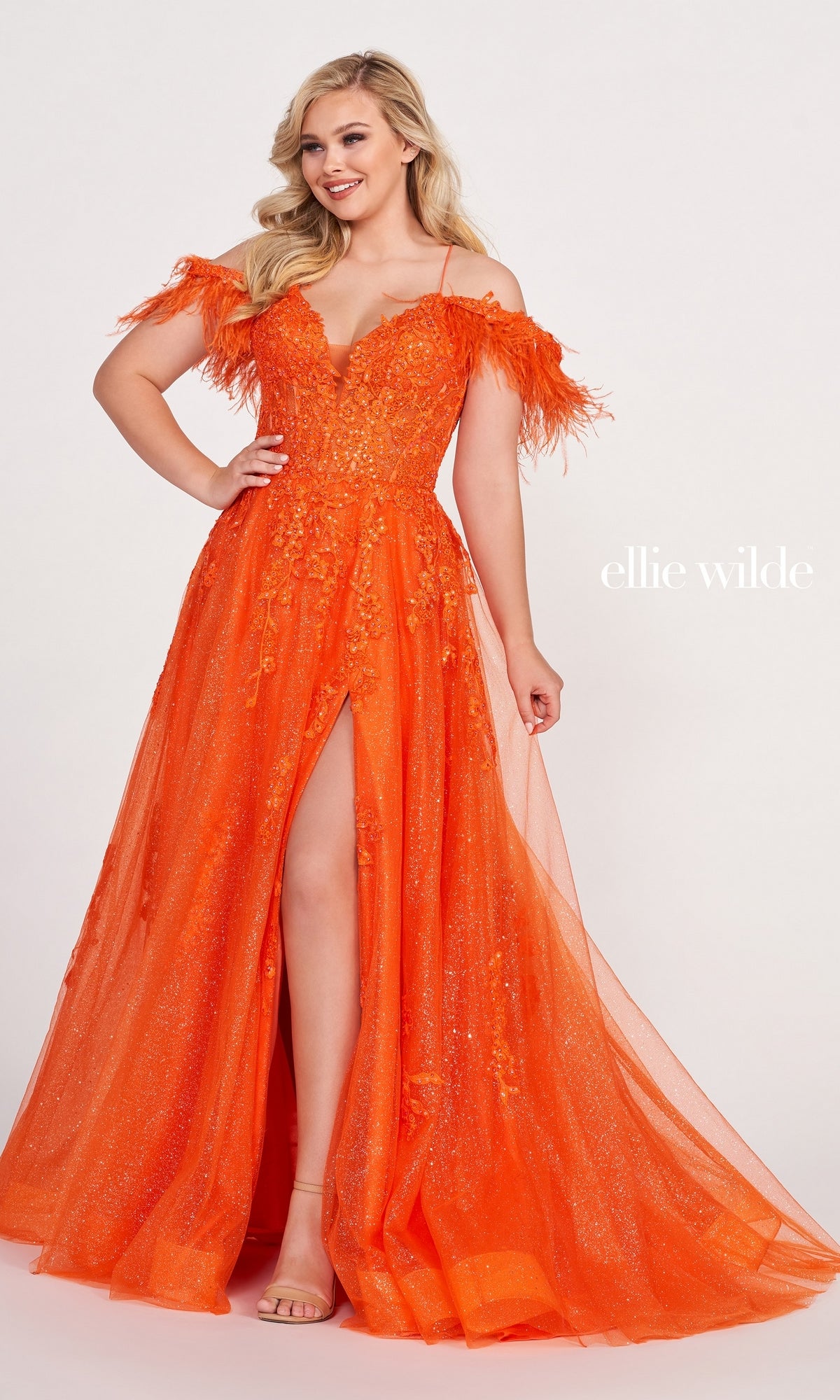 A woman models the Glitter Ball Gown With Off The Shoulder Feather Sleeves—featuring bright orange glitter, feathered sleeves, a thigh-high slit, and floral details—against a plain background.